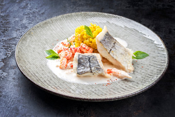 Fried haddock filet with saffron rice and shell prawns in crab sauce as closeup on a modern design plate