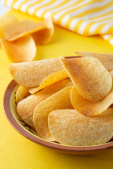 Potato chips in bowl on yellow background, top view
