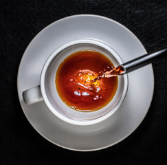 Coffee and cream pouring into a white cup on a white saucer with a black background