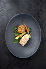 Fried Danish skrei cod fish filet with vegetable, lettuce and mushroom rice as top view on a modern design plate