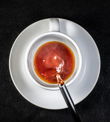 Coffee and cream pouring into a white cup on a white saucer with a black background
