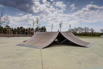Outdoor skatepark with various ramps  with a cloudy sky.