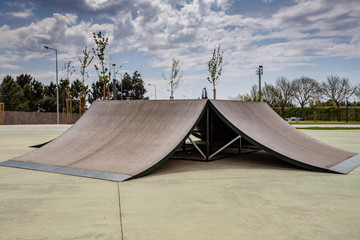 Outdoor skatepark with various ramps  with a cloudy sky.