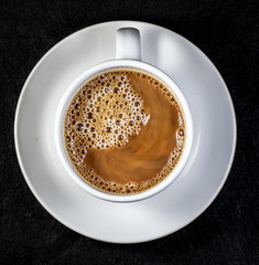 Coffee and cream pouring into a white cup on a white saucer with a black background
