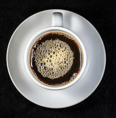 Coffee and cream pouring into a white cup on a white saucer with a black background