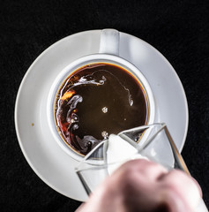 Coffee and cream pouring into a white cup on a white saucer with a black background