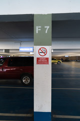 Red No smoking allower sign in three languages in an underground parking with cars visible in the background
