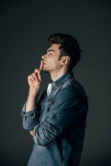 side view of handsome and brunette man in denim shirt showing shh gesture isolated on black