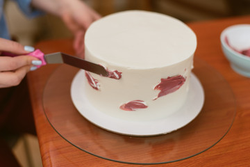 confectioner decorates white cake with color pink cream