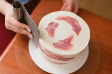 The confectioner levels the cream on the cake. The cook creates a cake, collects it and covers it with cream and then levels it with a spatula and a scraper.
