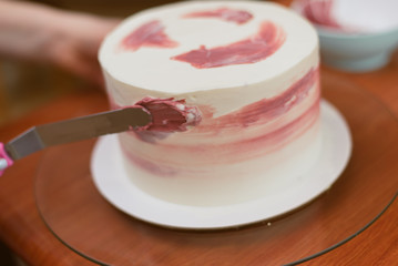 confectioner decorates white cake with color pink cream