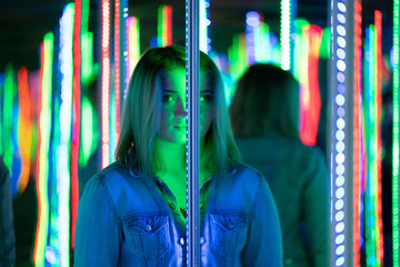sweet caucasian girl walks in a mirror maze with colorful diodes and enjoys an unusual attraction...