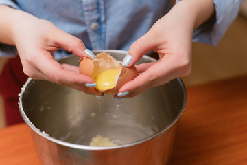 girl breaks an egg in a metal bowl for dough