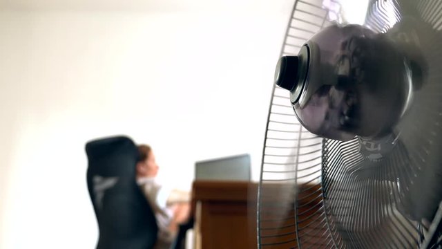 close-up of part of an office fan, on the background of a blurred writing desk, at which a person works at a computer
