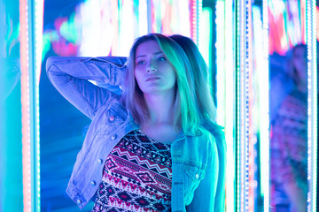 sweet caucasian girl walks in a mirror maze with colorful diodes and enjoys an unusual attraction room in the city