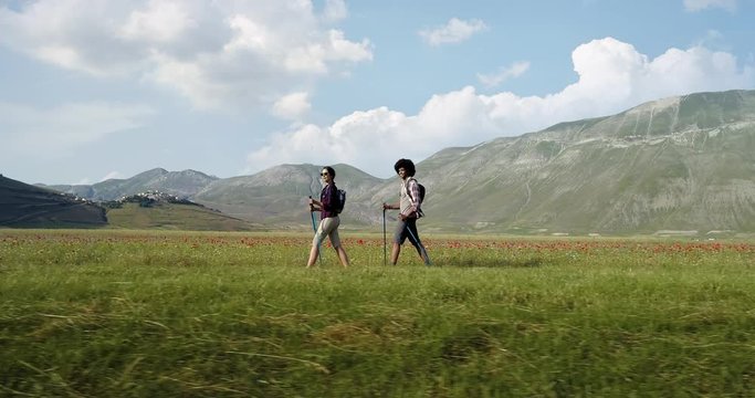 Aerial view flying above two people couple hiking or nordic walking outdoor on a trail path near flower fields in Castelluccio di Norcia. side follow. Friends italian trip in Umbria.4k drone