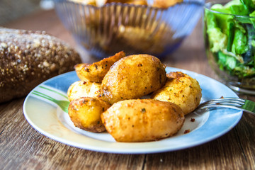 Baked young potatoes on a plate, homemade whole grain bread and lettuce salad on vintage wooden table