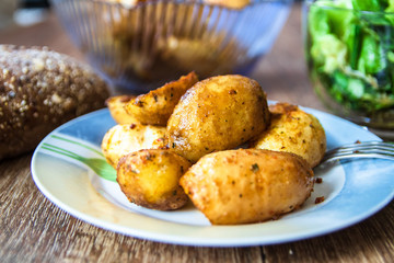 Baked young potatoes on a plate, homemade whole grain bread and lettuce salad on vintage wooden table
