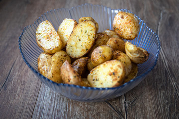 Baked young organic potatoes in a glass bowl on vintage wooden table