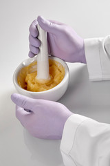 Closeup of the hands of a pharmacist or scientist, holding a mortar and pestle and wearing rubber gloves,pharmacist mixing medicine
