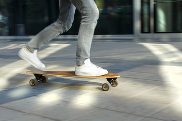 Fototapeta na wymiar Male skateboarder riding and practicing longboard in the city, outdoors, in motion, cropped image. Man down the street with skateboard. Leisure, healthy lifestyle, extreme sports concept