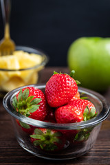 close up of fresh strawberries in a glass bowl served on wooden board with a dark background isolated from other fruits