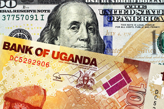 A close up image of a multi-colored Ugandan thousand shilling bank note with a blue American one hundred bank note in macro