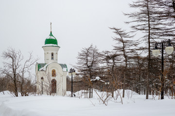 A small Christian chapel. Lots of snow in the park among the trees. Cold winter weather. Beautiful traditional Russian Orthodox architecture. Chapel of St. George. Magadan, Siberia, Far East of Russia