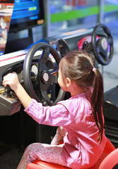 Little Asian kid girl playing arcade video game. Racing car.