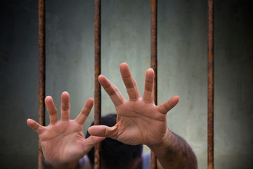 Man Hands of the prisoner desperate to catch the old prison rusted metal bars cell lock, concept of hope to be free and help