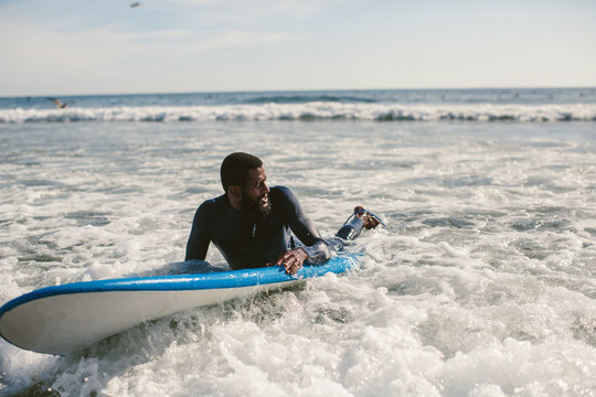 Handsome man has surfing on small waves. Mixed race dark skin and beard. Summer sport activity, white wash waves