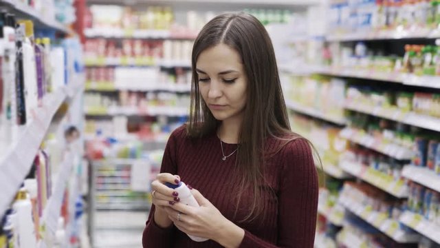 Girl chooses shower gel and sniffs it in cosmetics department at supermarket, emotion dislike
