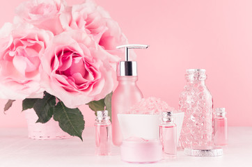 Obraz na płótnie Canvas Spa cosmetics products, roses in pastel pink and silver color - cream, bath salt, essential oil, soap, bottle, bowl, towel on white wood shelf.