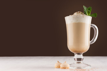 Coffee with cream, fresh mint, chocolate powder and cookies in irish coffee glass on dark brown and white wooden table, copy space.