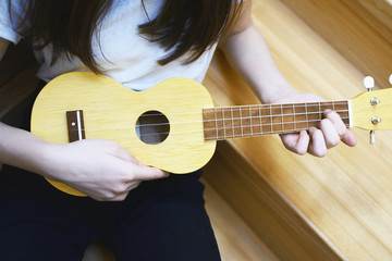 Girl hands playing song on yellow ukulele guitar. Music and hobbies concept.