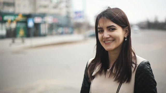 cute girl smiling to camera on the street with the view parked cars near big supermarket in the background