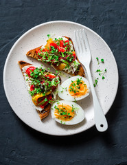 Healthy breakfast or snack - whole grain bread, feta, pickled pepper sandwiches and boiled egg on dark background, top view