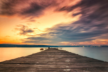 Fototapeta na wymiar Exciting sky with clouds at the shore with wooden pier and boat