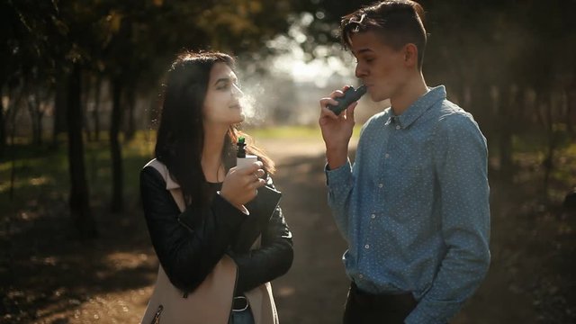 handsome vaping man talking with beautiful vaping girl in the park