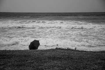 black and white photo of an umbrella lying on the shore of a stormy sea
