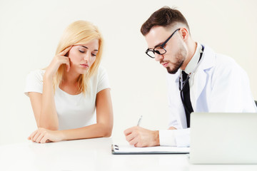 Male doctor talks to female patient in hospital office while writing on the patients health record...