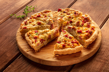 A photo of a quiche lorraine with thyme on a dark rustic wooden background