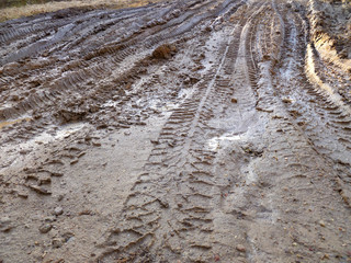 Tires deep tracks on a muddy road. Muddy dirt road in countryside with puddles filled with water and deep tracks from heavy vehicle.