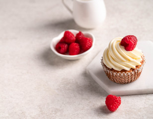 cupcake decorated with cream and raspberry on a marble board, light grate marble backdrop
