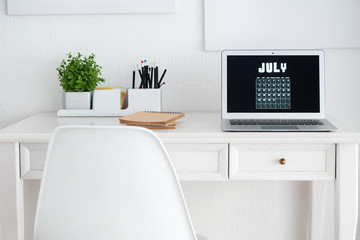 Comfortable workplace with stationery and laptop displaying calendar on screen
