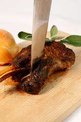 Lamb leg roast slow cooked displayed on wooden cutting board with big knife, onion and fresh mint leaves.