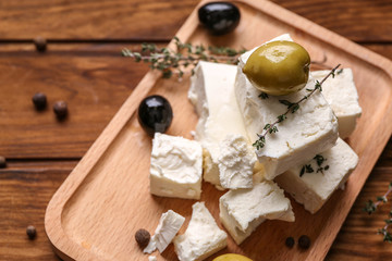 Plate with tasty feta cheese and olives on wooden table