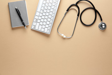 Stethoscope, computer keyboard and notebook on color background. Concept of online medical consultation
