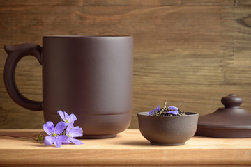 Set for tea ceremony. Large clay  cup (stein) with a lid, tea leaves and flowers. Front view.
