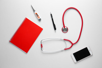 Stethoscope, notebook, mobile phone and thermometer on white background